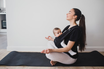 Young mother doing yoga with baby in ergo backpack