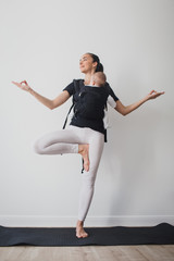 Obraz premium Young mother doing yoga with baby in ergo backpack