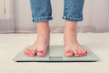 Person is weighed on scales, female feet, cropped image, front view, toned
