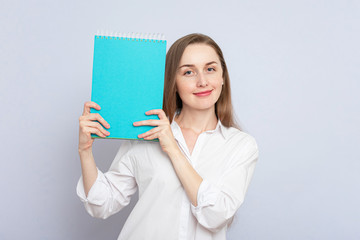 Young girl shows blue notebook and smiles, copy space