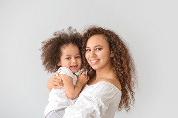 Little African-American girl with her mother on light background