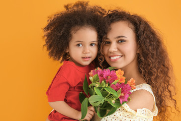 Little African-American girl with her mother and bouquet on color background