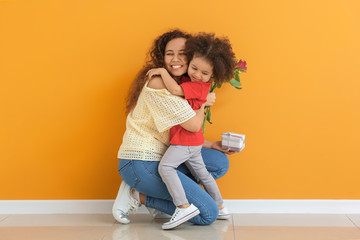 Little African-American girl greeting her mother near color wall
