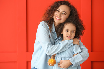 Little African-American girl with her mother on color background