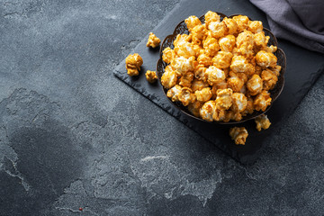 Popcorn in caramel glaze in a plate on a dark concrete table. Copy space.