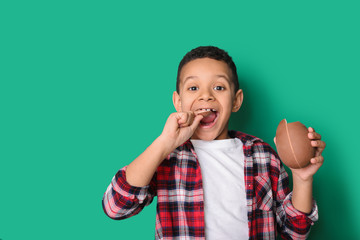 Cute African-American boy with sweet chocolate egg on color background