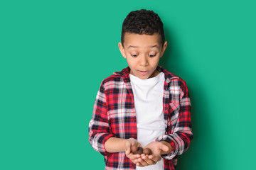 Surprised African-American boy with sweet chocolate eggs on color background