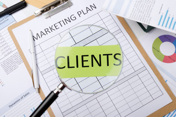 Concept of getting new clients and making marketing plan to increase sales.Magnifying glass, word clients on the green paper, office desk and documents on it