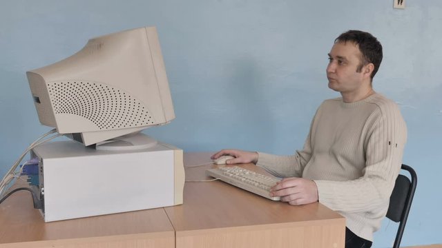 Man playing computer game on the old computer, he puts his feet on the table and is getting comfortable 