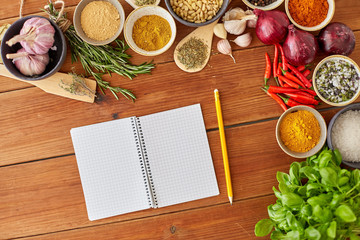 food, culinary and eating concept - notebook with pencil among different spices, onion, garlic with pine nuts and red hot chili peppers on wooden table