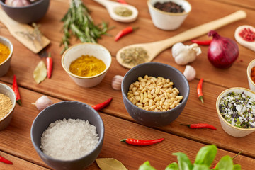 food, culinary and eating concept - bowls with different spices, onion, garlic with pine nuts and red hot chili pepper on wooden table