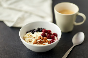 food and breakfast concept - porridge in bowl with wild berries, almond nuts, spoon and cup of coffee on slate stone table