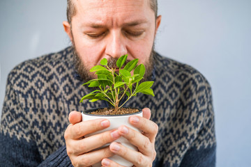 Bearded man in sweater holding and smelling the plant in hands, shallow debt of field