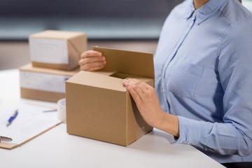 delivery, mail service, people and shipment concept - close up of woman packing parcel box at post office