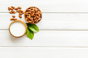 Almond milk near nuts on white wooden background top-down copy space