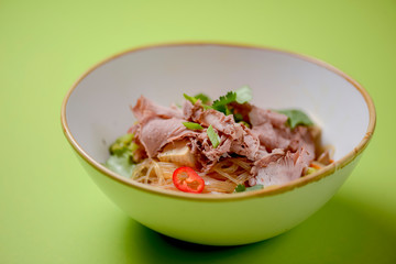 Rice noodles with beef and vegetables served in a white bowl over bright green background.