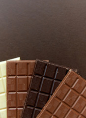 sweets, confectionery and food concept - milk, dark and white chocolate bars on brown background