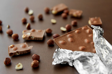 sweets, confectionery and food concept - milk chocolate bar with hazelnuts in foil wrapper on brown background