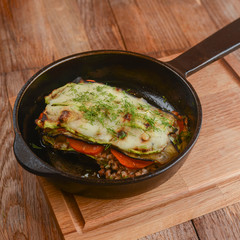 Backed eggplant with mozzarella cheese, tomatoes and basil served in a pan over rustic wooden board in a restaurant.