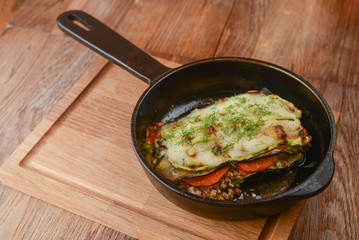 Backed eggplant with mozzarella cheese, tomatoes and basil served in a pan over rustic wooden board in a restaurant.