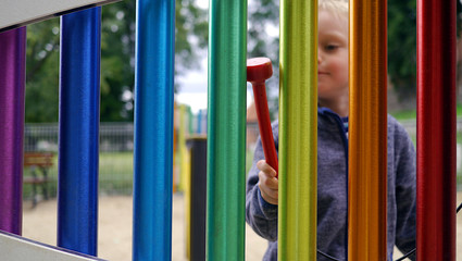 Dziecko na placu zabaw gra na cymbałkach. Stoi z mamą przy kolorowym xylophones. Chłopiec gra na...