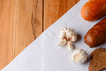 Different kinds of bread with fresh raw garlic on white tablecloth over light rustic wooden table.