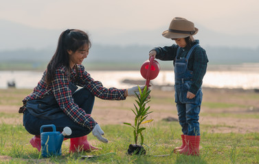 Asian little girl with mom planting and watering tree in nature. First learning of little children.