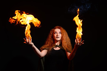 Portrait of a Halloween witch imposes a flame spell. Beautiful redhead woman doing witchcraft holds...