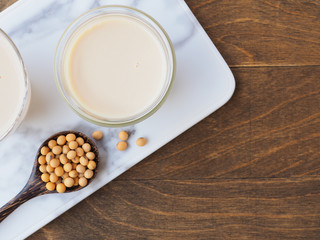 Obraz na płótnie Canvas Soy milk in a glass cup with a wooden spoon on a white cutting board over wooden background. Top view with copy space. Plant protein.