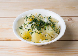 Boiled potatoes with dill in a white bowl on the boards. Side view