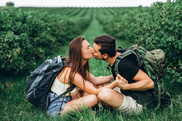 Man and woman with backpacks on their backs sitting hugging on the green grass between the currant bushes. Walking on the currant plantations in the countryside