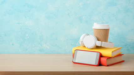 Headphones, smartphone, stack of books and paper cup on a table