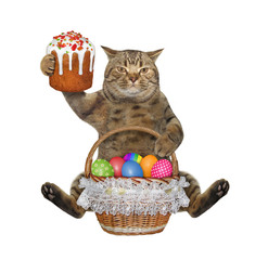 The beige cat is sitting with a easter cake and a wicker basket of colorful eggs. White background. Isolated.