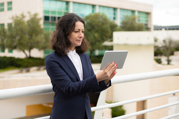 Smiling businesswoman using tablet computer. Content middle aged businesswoman using digital tablet while standing on urban city street. Wireless technology concept