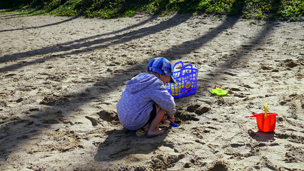 Dziecko bawi się na plaży obok molo. Chłopiec bawi się samochodami budowlanymi - koparka i wywrotka. © Marcin