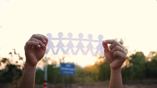 Teamwork concept with paper chain group of people holding hands held in the park over sunset background.