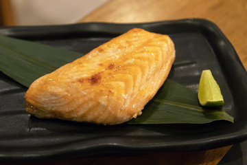Grilled salmon steak on black plate with lime.