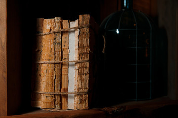 Old books, rewound with a rope, stand on a wooden shelf. 