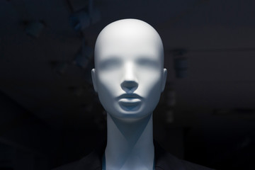 A close-up of a mannequin’s head in a window of a mall on the dark background with switched off...