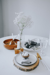 Easter table setting with white plate, gray textile napkin, candles, quail and chicken eggs and blossom branch.Mock up easter card