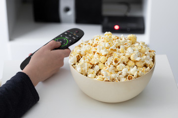 Hand holding tv remote control  and popcorn bowl.Watching Tv at home