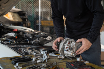 Mechanic man holding alternator of the car on working table in repair and maintenance garage - obrazy, fototapety, plakaty
