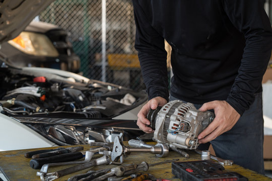 Mechanic Man Holding Alternator Of The Car On Working Table In Repair And Maintenance Garage