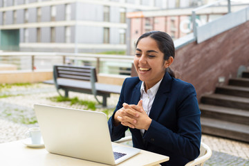 Fototapeta premium Happy businesswoman using laptop in cafe. Cheerful young businesswoman sitting at table and using laptop computer in outdoor cafe. Business and technology concept