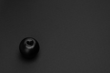 Black apple on the matte black background. Minimal style. Conceptual minimalist black art. Matte surface. Fruit. One. Space for text