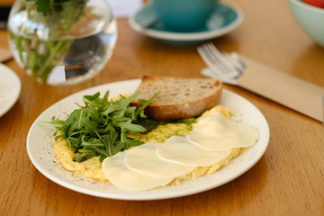 Healthy breakfast in the cafe. Egg omelet with cherry tomatoes decorated with arugula in a white plate on a wooden table. 