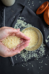 A scattering of rice, a handful of rice, rice in a metal bowl on a dark background. 