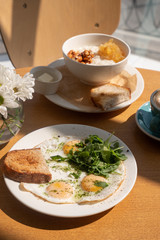Tasty healthy breakfast: fried eggs, salmon, arugula and croutons on a white plate and  a mug of cappuccino on a wooden table.