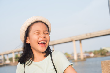 asia little girl with city map on summer vacation. travel and adventure concept, outdoor portrait girl  in hat  traveling around a happy smile and laughing child girl. town by the river.