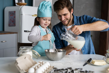 Daddy with daughter baking cake together in home kitchen.